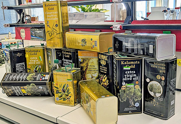 Das Bild zeigt zahlreiche Oliven�lproben, �berwiegend gro�e 5-Liter-Kanister, die auf einem Labortisch gestapelt sind. Die als �Natives Oliven�l Extra� ausgelobten Produkte sind qualitativ hochwertig aufgemacht, werben mit Herkunftsangaben oder loben bestimmte Qualit�tskriterien besonders aus. Bei allen abgebildeten Proben handelt es sich dabei um Produktf�lschungen.