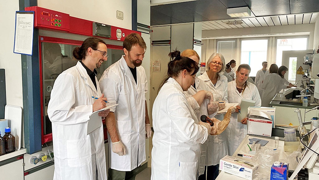 Eine Personengruppe steht im Labor und es wird die Aufarbeitung von Fischen für die MALDI-TOF MS Messung demonstriert.